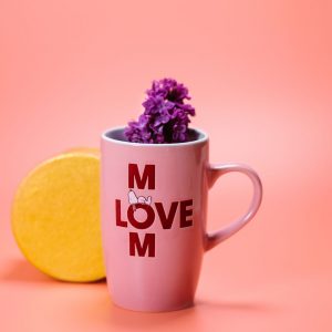 Tienda Pink mug with 'Love Mom' text and purple flowers, perfect for Mother's Day on a pink background.